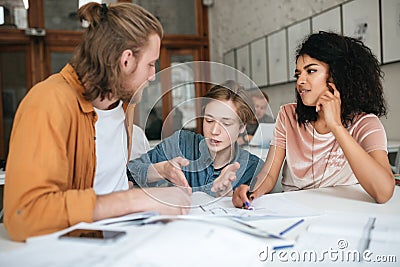 Young people emotionally discussing something in office. Two boys with blond hair and girl with dark curly hair sitting Stock Photo