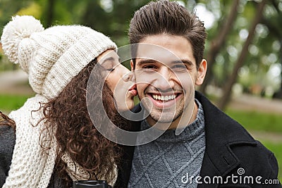 Portrait of young people man and woman 20s smiling and kissing, while sitting on bench in green park Stock Photo