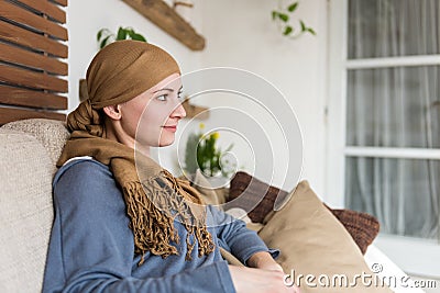 Portrait of young positive adult female cancer patient sitting in living room, smiling. Stock Photo