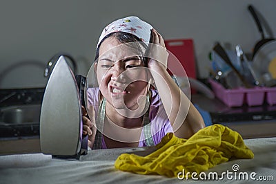 Portrait of young pretty frustrated and stressed Asian Chinese woman working at home kitchen ironing clothes desperate and overwhe Stock Photo