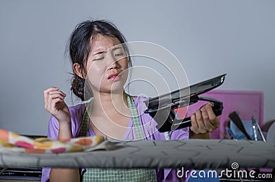 Portrait of young pretty frustrated and stressed Asian Korean woman holding iron working at home kitchen ironing clothes desperate Stock Photo