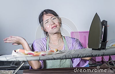 Portrait of young pretty frustrated and stressed Asian Korean woman working at home kitchen ironing clothes desperate and overwhel Stock Photo