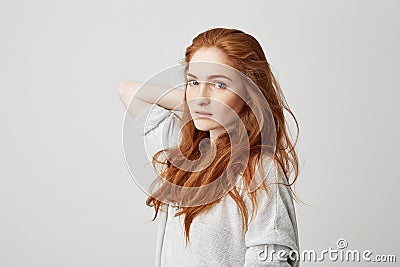 Portrait of young pretty ginger girl with freckles looking at camera touching hair over white background. Stock Photo