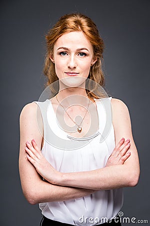 Portrait of a young redhaired beautiful girl in the studio on a gray isolated background. A woman is standing with her arms folded Stock Photo