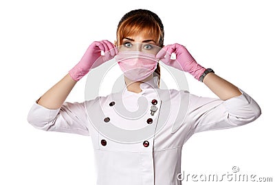 Portrait of young red-haired woman doctor or nurse in white medical uniform and gloves putting protective mask on face Stock Photo
