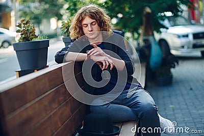 Red haired hipster man sitting on bench looking to his watch Stock Photo