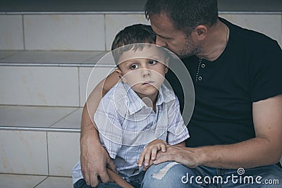 Portrait of young sad little boy and father sitting outdoors at Stock Photo