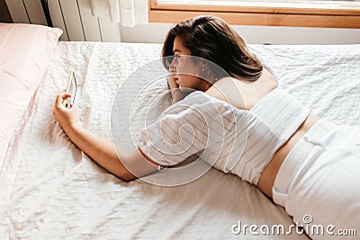 Portrait of young sad woman lying on the bed looking smartphone feels unhappy. Waiting for mobile message. Feeling worried, hurt, Stock Photo