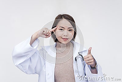 Portrait of a young and skilled doctor, medical student, intern pointing at her head with her thumbs up. Isolated on a white Stock Photo