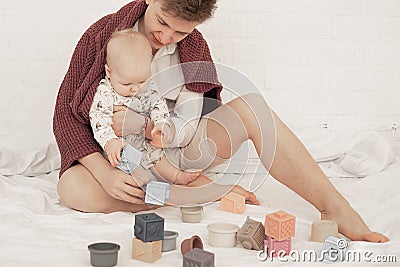 Portrait of young smiling father dad covered with plaid holding little plump baby, playing modern pastel silicone bowls. Stock Photo