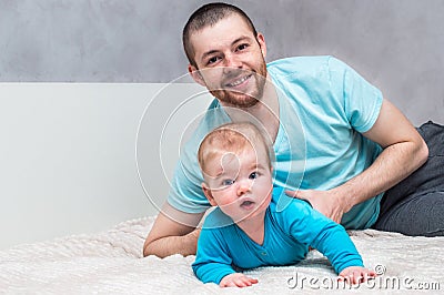 Portrait of a young smiling father with his infant in blue clothes on the bed in an embrace. Father`s day concept Stock Photo