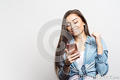 Portrait of young smiling woman with pink smartphone receiving some great news over white background. Lifestyle, people and techn Stock Photo