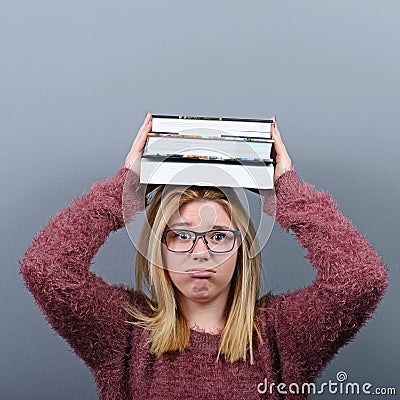 Portrait of a young student woman holding books on head against gray background.Tired of learning/studying concept Stock Photo