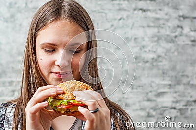 Portrait of young teenager brunette girl with long hair eating burger. Girl trying to eat fast food Stock Photo