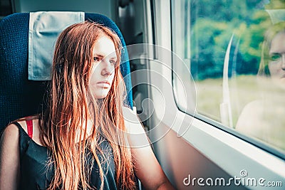 Young teenager redhead girl with long hair looks out the window while sitting in the train. Stock Photo