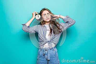 Portrait of young upset puzzled woman student in denim clothes hold alarm clock isolated on blue background. Time is running out. Stock Photo