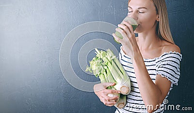 Portrait of a young woman with a bunch of celery in one hand and a glass of celery juice in the other. dark background, studio Stock Photo