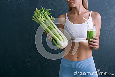 Portrait of a young woman with a bunch of celery in one hand and a glass of celery juice in the other. dark background, studio Stock Photo