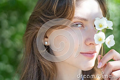 Portrait of a young woman close-up, covering her eye with a branch of jasmine. Beautiful smiling girl with flower in her Stock Photo