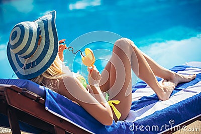 Young woman with cocktail glass chilling in the tropical sun near swimming pool on a deck chair Stock Photo