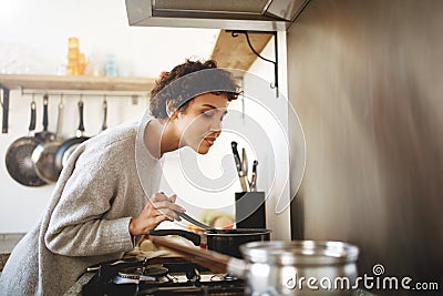 Young woman cooking and smelling food from pot Stock Photo