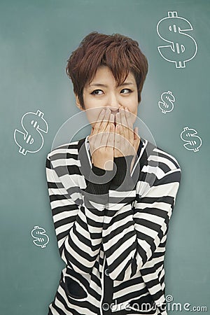 Portrait of young woman covering her mouth in front of blackboard with dollar signs Stock Photo