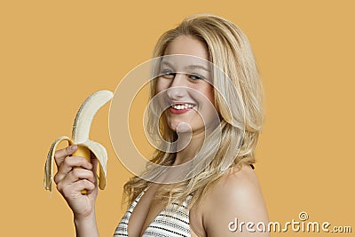 Portrait of a young woman eating banana over colored background Stock Photo