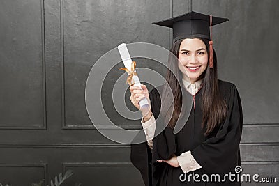 Portrait of young woman in graduation gown smiling and cheering on black background Stock Photo