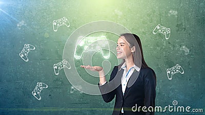 Portrait of young woman holding gamer`s joystick on the open hand palm, over drawn studio background. Business concept. Stock Photo