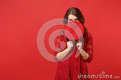 Portrait of young woman in lace dress hiding, covering face with cap, looking aside isolated on bright red wall Stock Photo