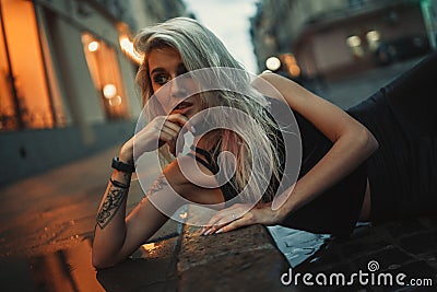 Portrait of young woman lying on wet pavement on city street in Stock Photo