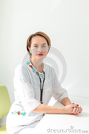 Portrait of a young woman professional doctor with short haircut, in a bright medical room, in a white coat with a phonoscope on Stock Photo