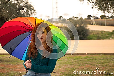Portrait of young woman, red hair, freckles, with a rainbow umbrella, happy, in an outdoor park. Concept color, happiness, well- Stock Photo