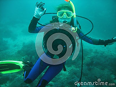 The portrait of young women scuba diver under water. She is in full scuba diving equipment: mask, regulator, BCD. She is showing O Stock Photo