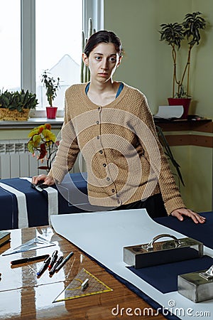 Portrait of a young woman seamstress in a home Studio. Looks appraisingly at client. Holding a pair of scissors. Handmade concept Stock Photo