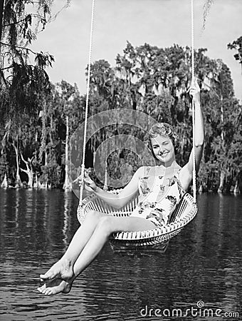 Portrait of a young woman sitting on a swing at the lakeside and smiling Stock Photo