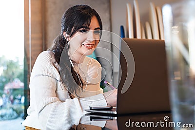 Portrait of young woman sitting at table in front of laptop. Girl works on computer cafe, checks e-mail, browses social networks Stock Photo