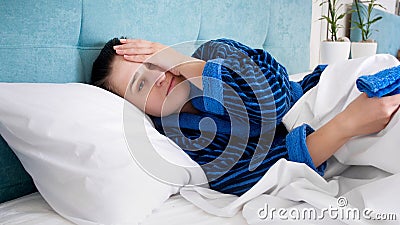 Portrait of young woman suffering from migrain headache lying in bed Stock Photo