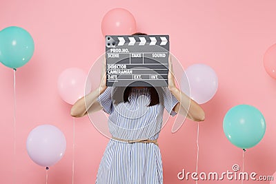 Portrait of young woman wearing blue dress covering face with classic black film making clapperboard on pink background Stock Photo