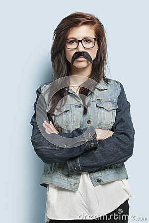 Portrait of young woman wearing eyeglasses and fake mustache against light blue background Stock Photo