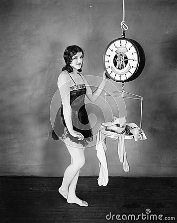 Portrait of a young woman weighing her clothes and sandals on a weighing scale Stock Photo