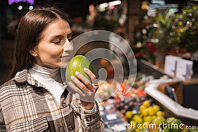 Portrait of a young woman who sniffing fresh mango in a supermarket. Girl buys fruit at the grocery store. Stock Photo