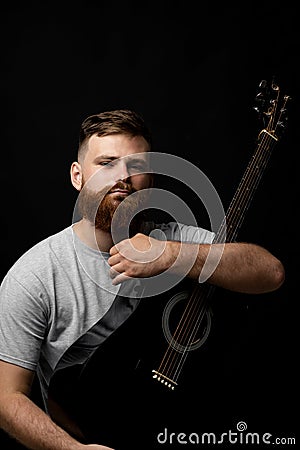 Portraite of bearded handsome musician holding a guitar in a dark room. Guitarist, artist, composer, rocker, star. Stock Photo