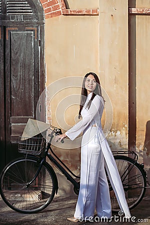 Portraits, beautiful women in traditional Vietnam national costumes Walking the bike out of her house Stock Photo