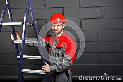 Portriat of man wearing overalls with step ladder near brick wal Stock Photo
