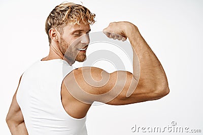 Portrit of handsome male athlete rear view, flexing biceps and smiling, showing strong arm after workout in gym, white Stock Photo