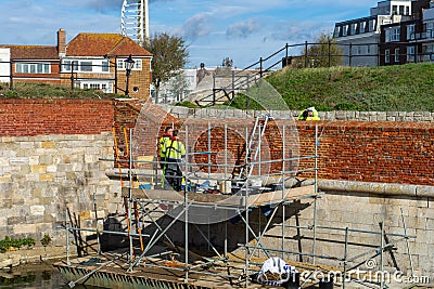 Bricklayers working on repairing a brick wall standing on scaffolding wearing harnesses Editorial Stock Photo