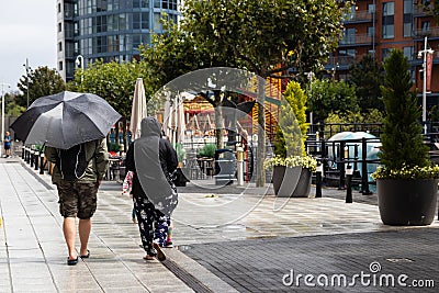 A couple walking in the rain, the lady is holding an upbrella Editorial Stock Photo