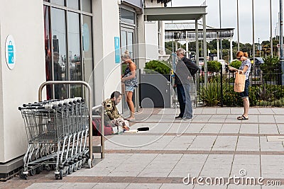 People queue for a cashpoint or ATM while a homeless man sits on the floor next to them Editorial Stock Photo