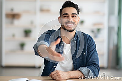 Positive arab man in casual sitting at workdesk, giving hand Stock Photo